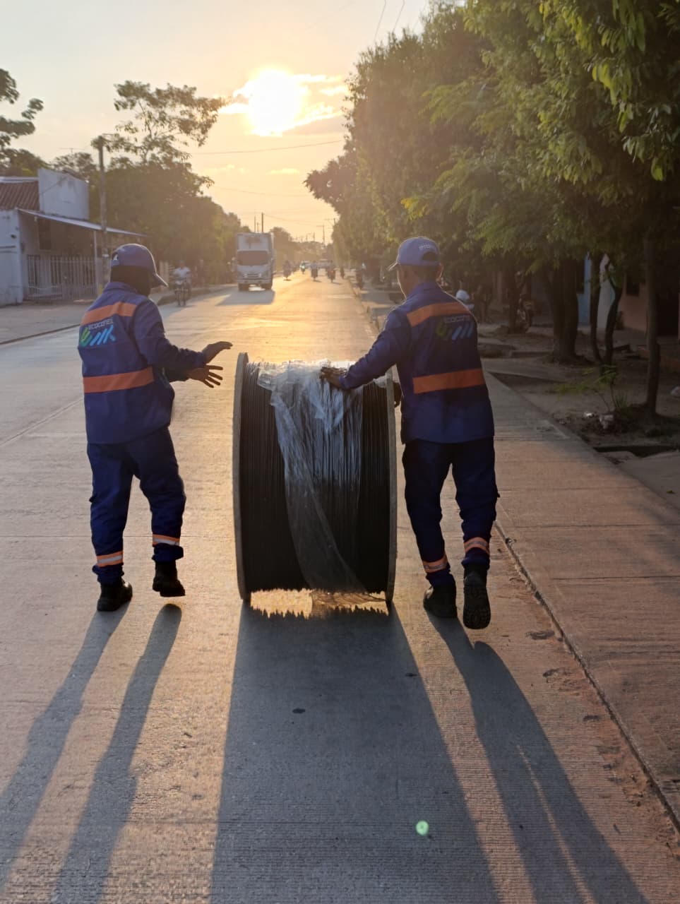 Técnicos de Ecoconex llevando bobina de cable de fibra óptica al atardecer en San Marcos